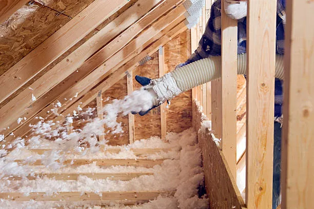 Loose-fill insulation being blown into an attic between wood rafters
