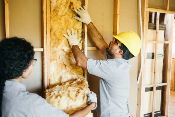 Two workers fitting fiberglass insulation into wall framing