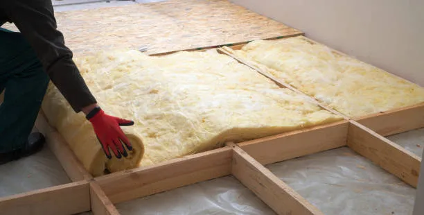 Fiberglass insulation being placed between horizontal wood joists
