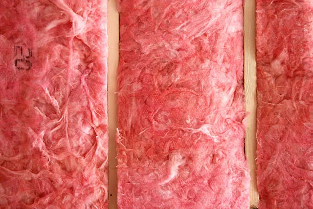 Pink fiberglass batts fitted between vertical wood wall studs