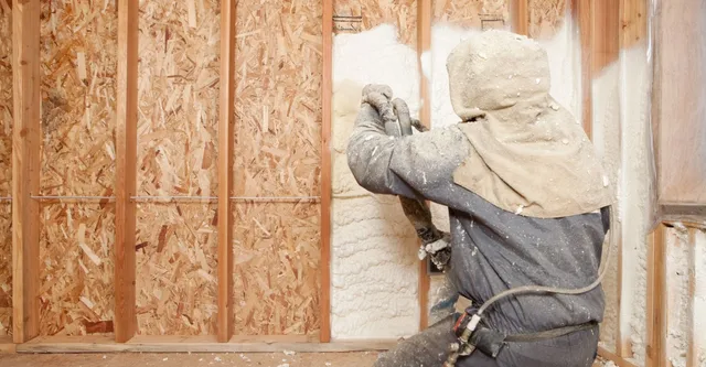 Worker applying spray foam insulation to an open wall cavity