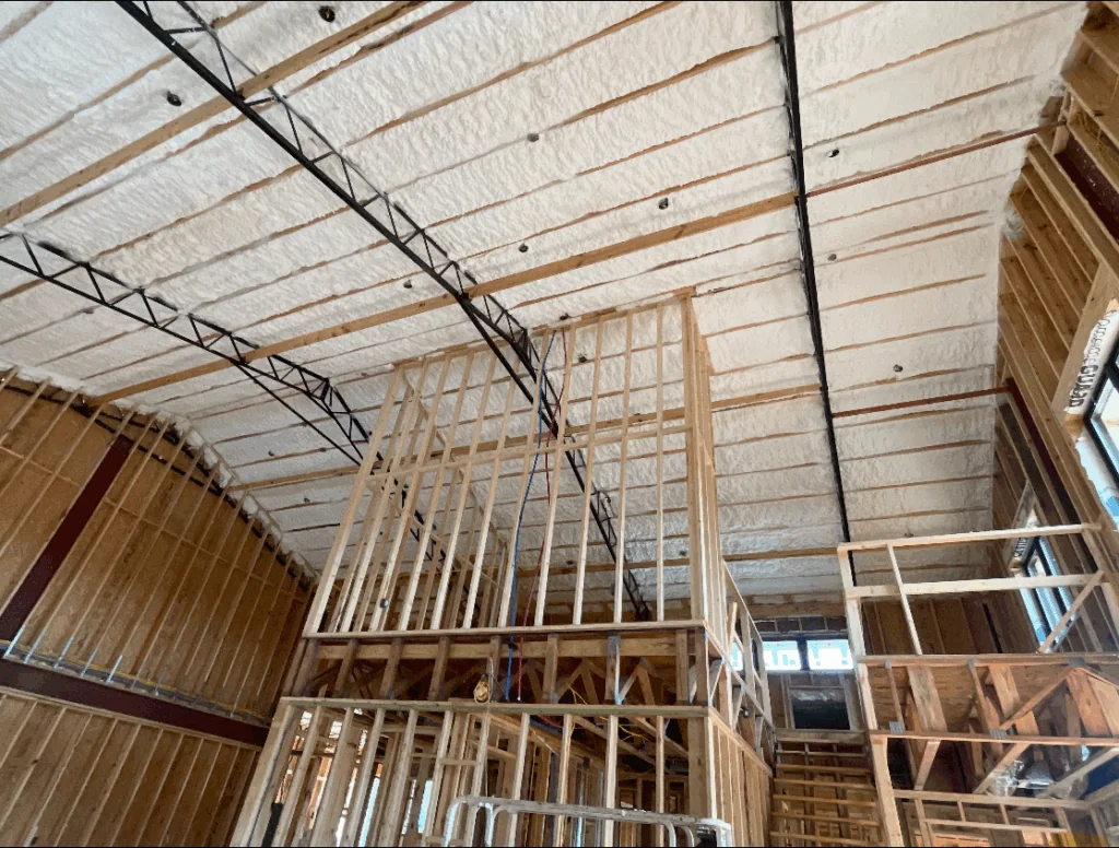 Spray foam insulation covering roof decking above exposed wall framing